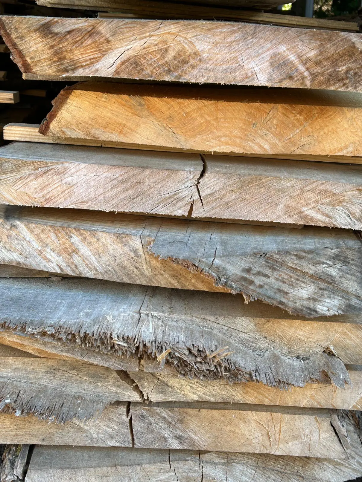Stack of weathered wooden planks with visible cracks and rough edges.