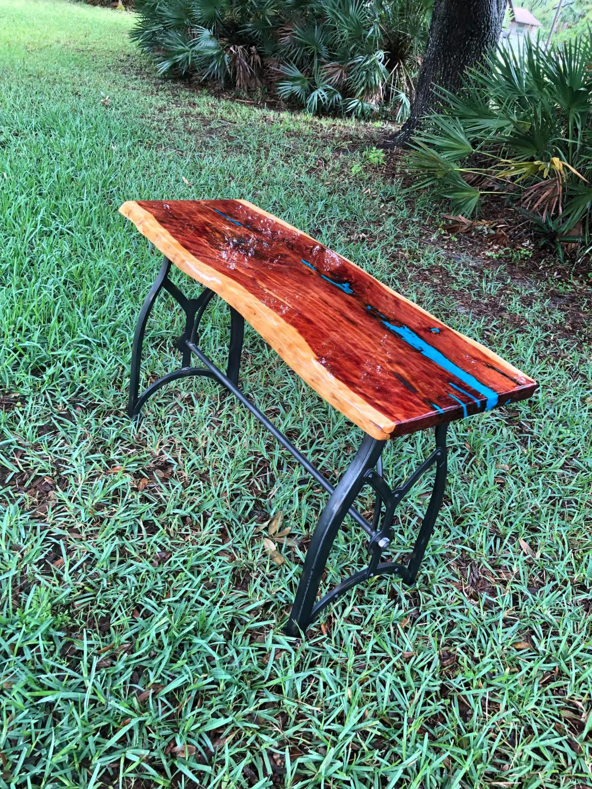 Handcrafted wooden bench with resin river design and metal legs on grass.