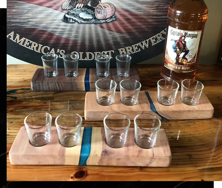Wooden flight board with six whiskey samples and a bottle on a bar counter.
