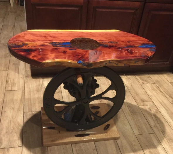Artistic side table with a wooden and resin top and metal wheel base.